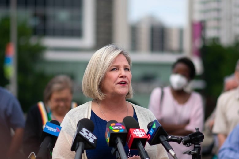 Photo of a woman in a beige blazer speaking to media