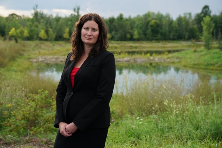 A woman in a suit poses in a field with her hands crossed in front of her.