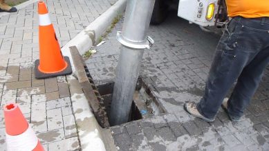 Stormwater maintenance happening on a side walk. Pylons and a pipe big in the stormdrain are in the photo