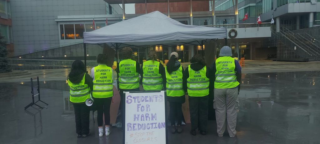 Students wearing vests that say "students against harm reduction" on the back.