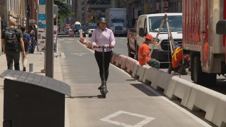 A woman on an electric scooter in a bike lane in a city street. Other people are seen in the background.