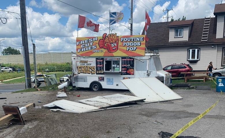 A chip truck is parked in a parking lot in the day time in summer. Police tape and debris surrounds it. A propane tank is lying at an angle behind it