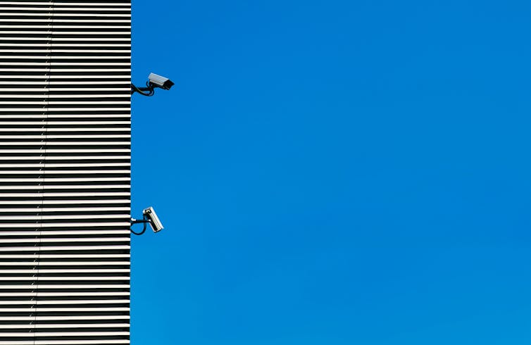 Two surveillance cameras on the side of a building against a blue sky.