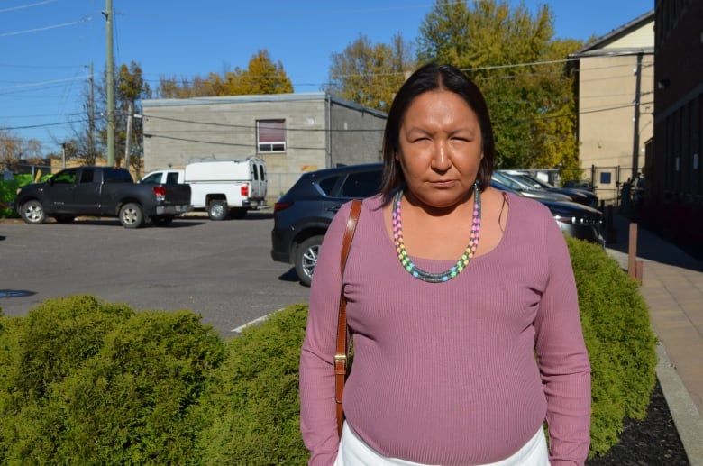 A woman stands in front of a parking lot, looking into the camera. 