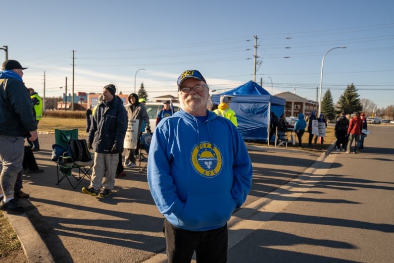 A man with glasses and grey beard smiles in front of protestors.