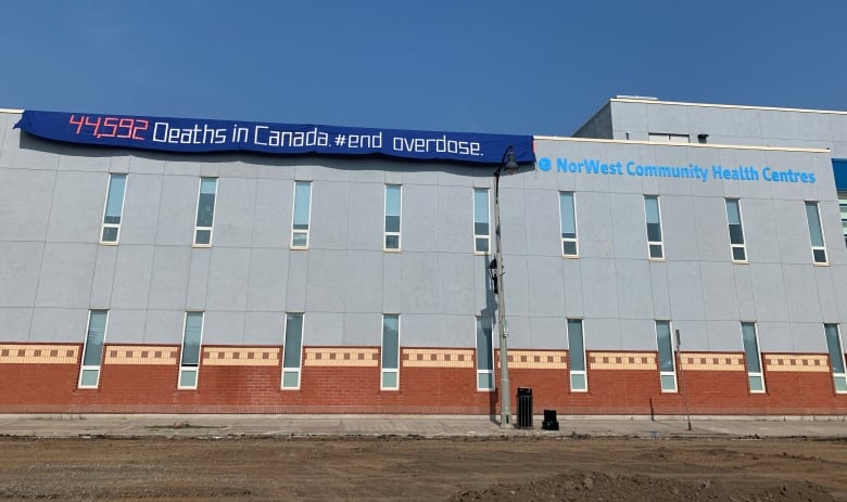 A wide shot of a building. A banner is draped over the building's roof that says "44,592 Deaths in Canada #end overdose."