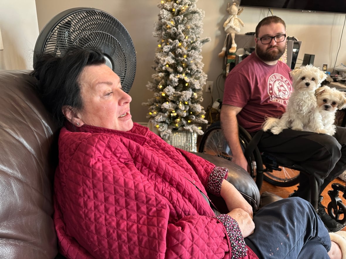 A woman seated on a couch while a man in a wheelchair looks on.