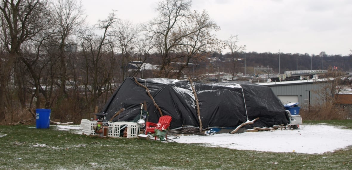 A tent covered in a black tarp surrounded by a plastic chair and a fence.