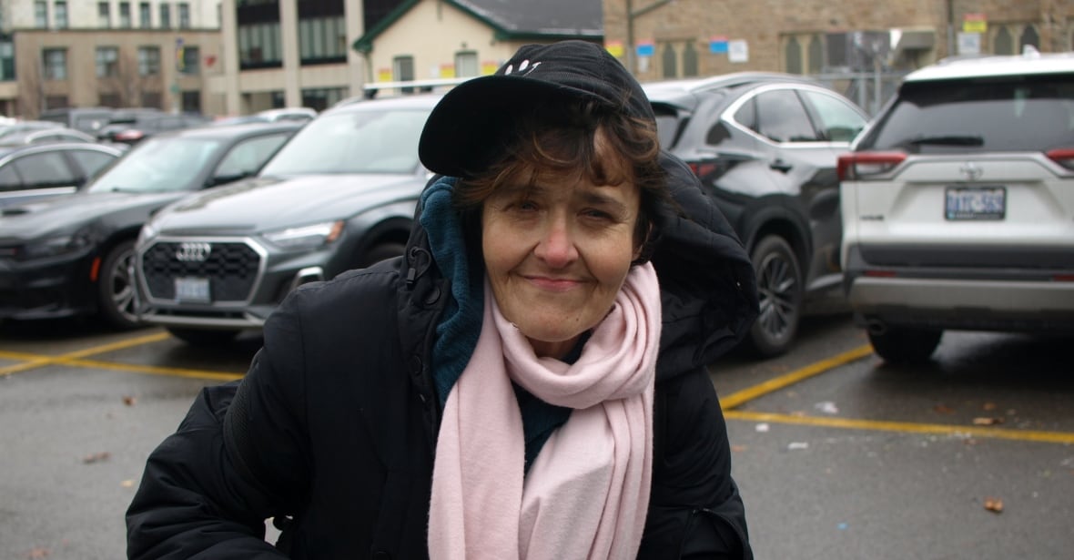 A person with a baseball cap and scarf smiles and squints