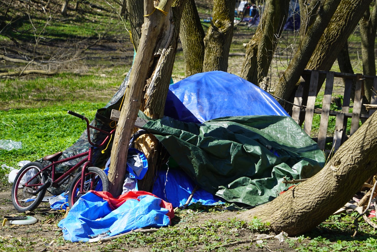 A blue crumpled tent nestled at the base of a tree surrounded by tarps and a small bicycle. 