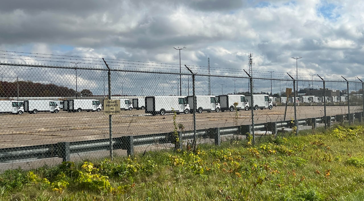 A long line of newly assembled BrightDrop delivery vehicles sit in a parking lot outside of GM's CAMI assembly plant.