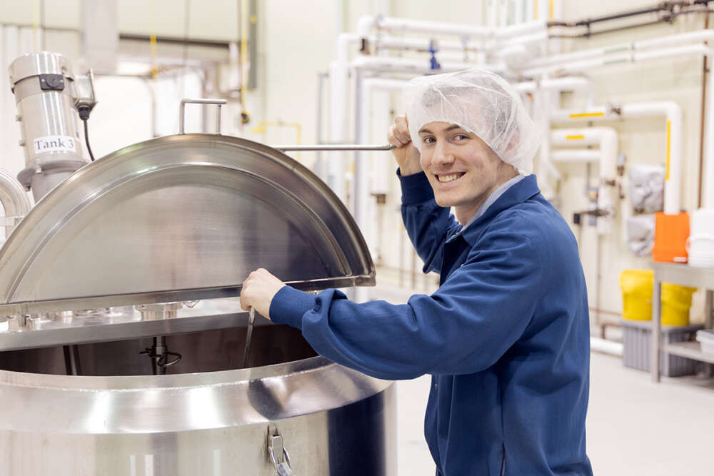 A food science co-op student wears a hairnet and mixes a giant vat in an industrial kitchen