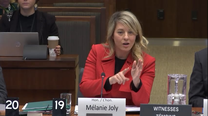 A woman in a red jacket speaks while sitting at a table