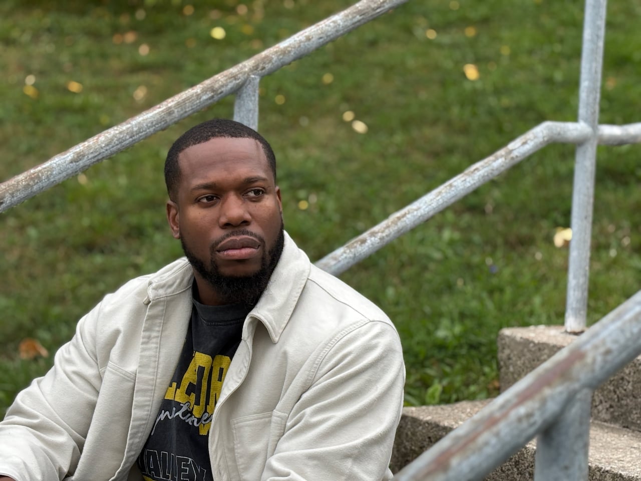 A black man, looks off into the distance, sitting on some bleachers