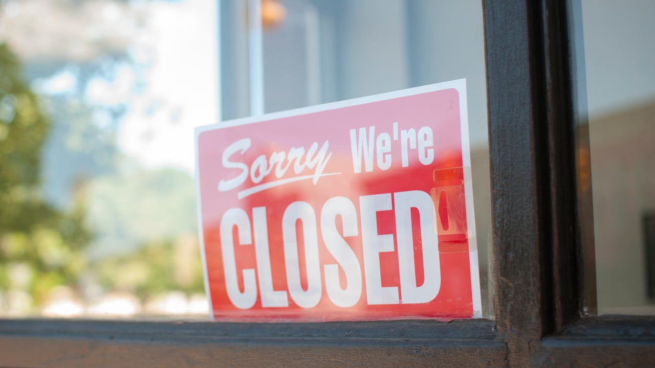 A red sorry we're closed sign behind a glass window.