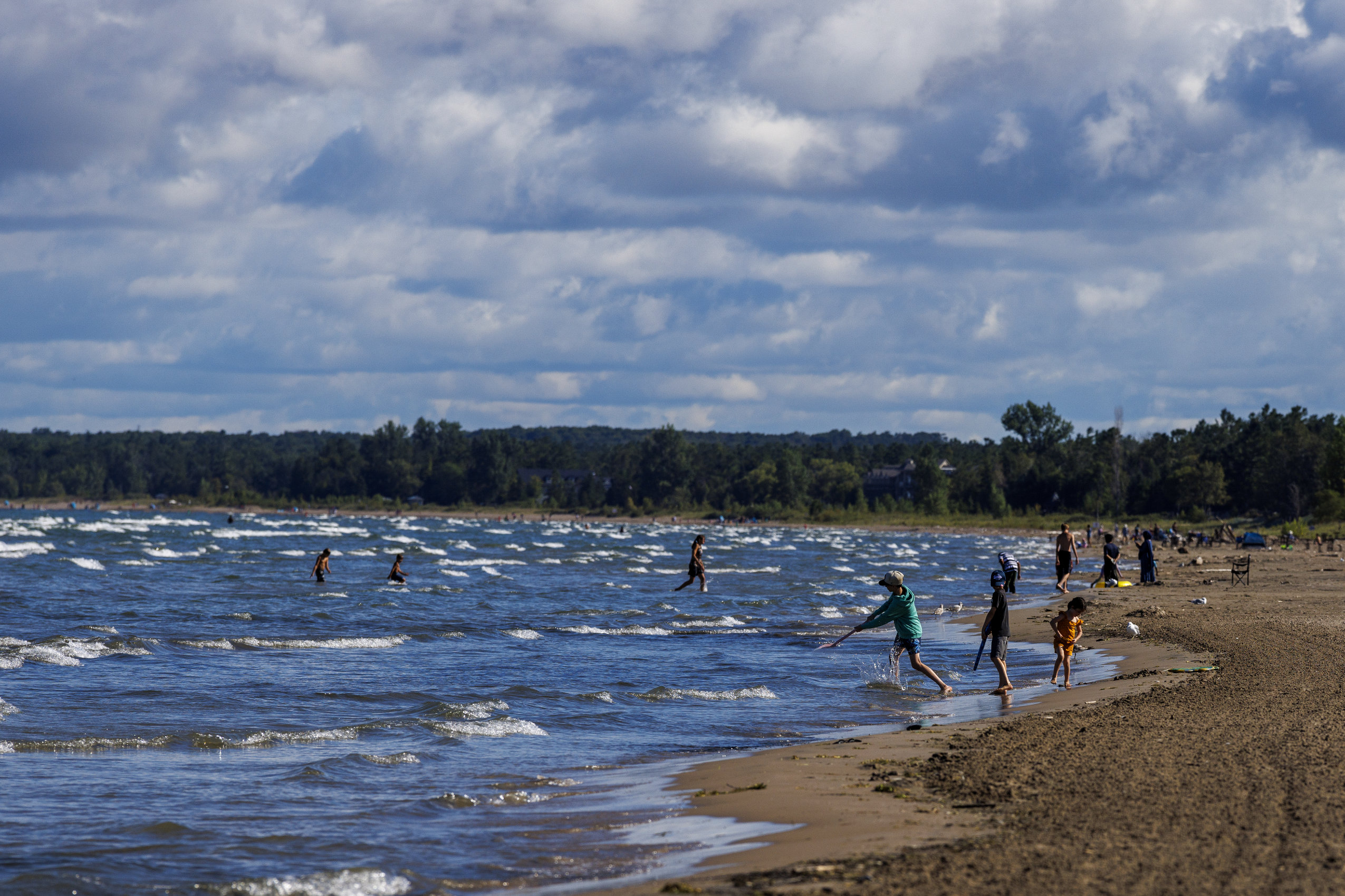 Bathers play in the water at Wasaga Beach as whitecap waves roll into shore.