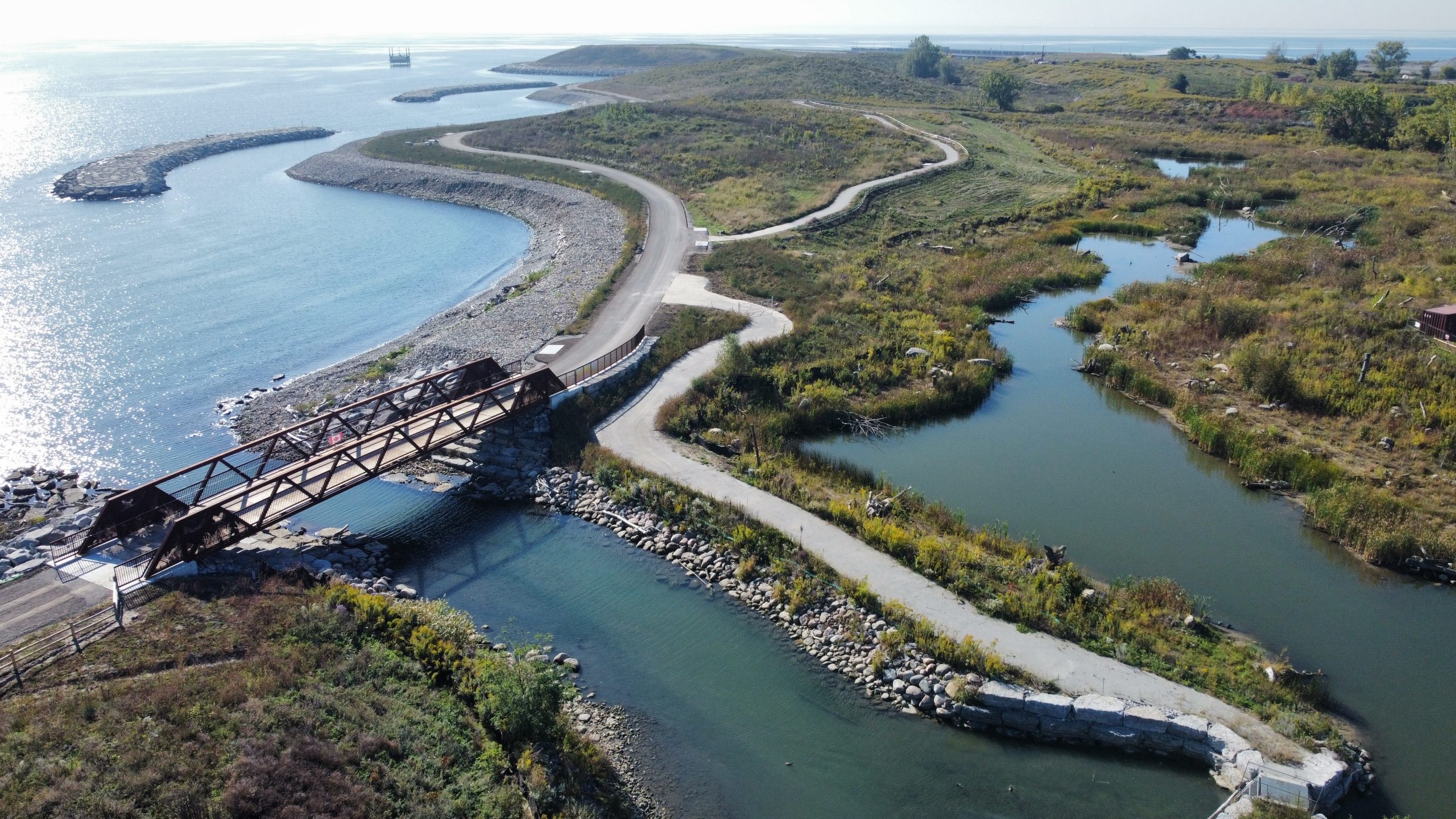The pedestrian bridge at Jim Tovey Lakeview Conservation Area connects visitors across restored aquatic channels and wetlands along the Lake Ontario shoreline. Designed as part of the conservation area's accessible trail network, it links visitors to habitat features like coastal wetlands fish habitat areas plus a 170-metre wetland boardwalk.