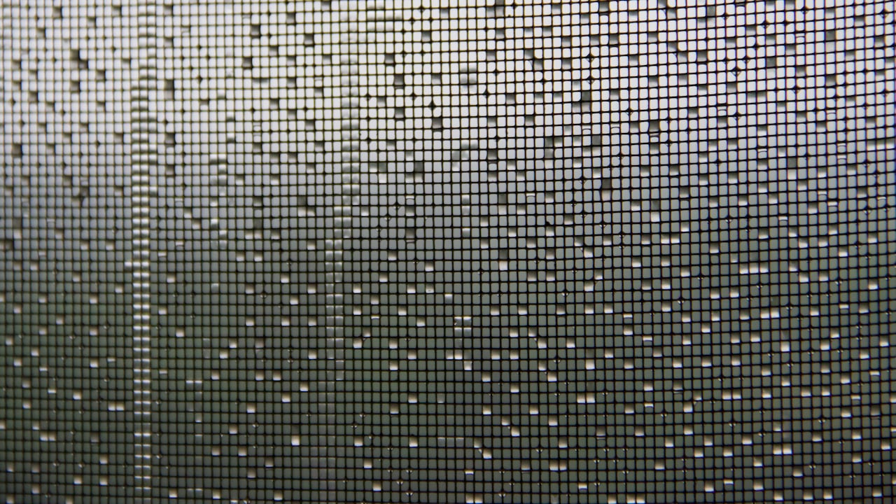 A closeup of a window screen with rain dripping down it
