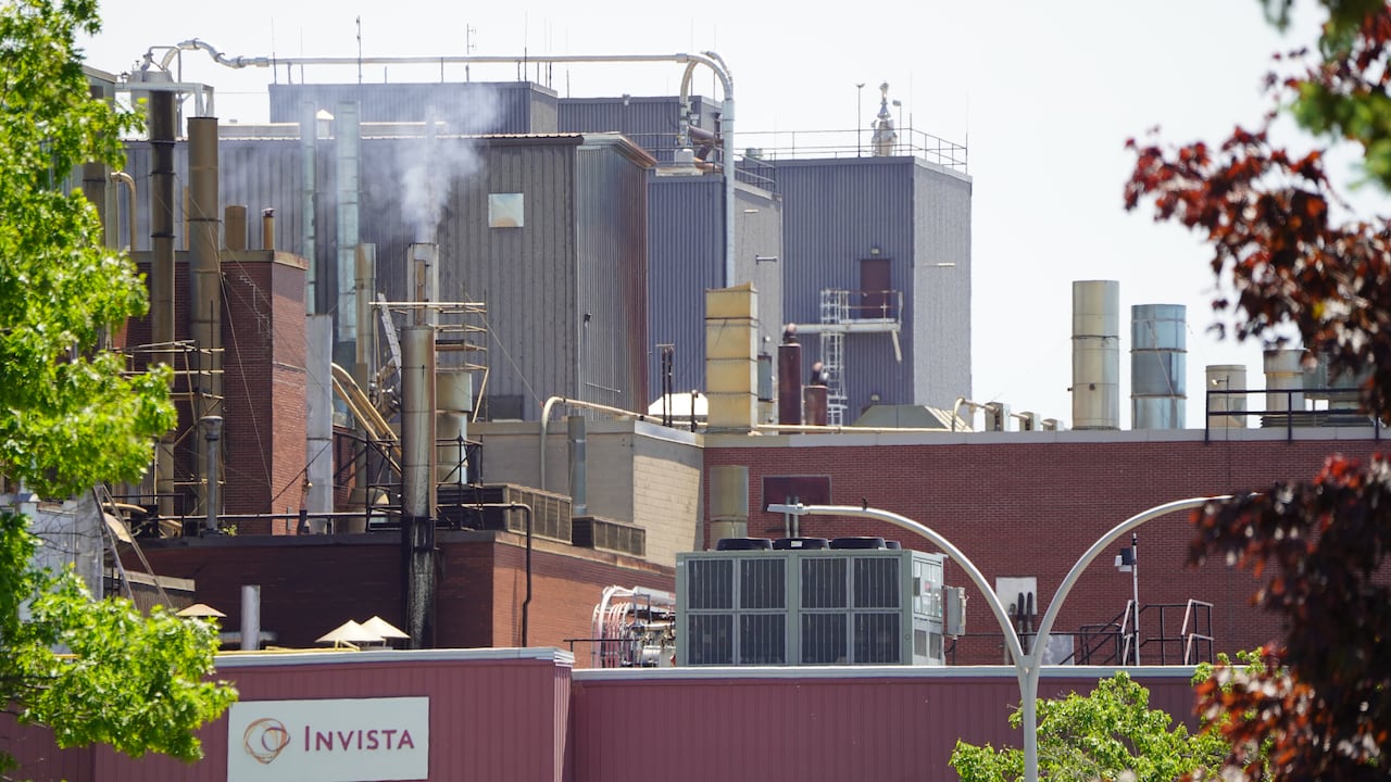 Pipes and exhaust stacks are seen on a red-brick plant building on a sunny day.