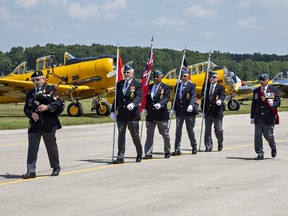 A colour guard from the Royal Canadian Legion Branch 153 Tillsonburg marches in front of a row of Harvard aircraft