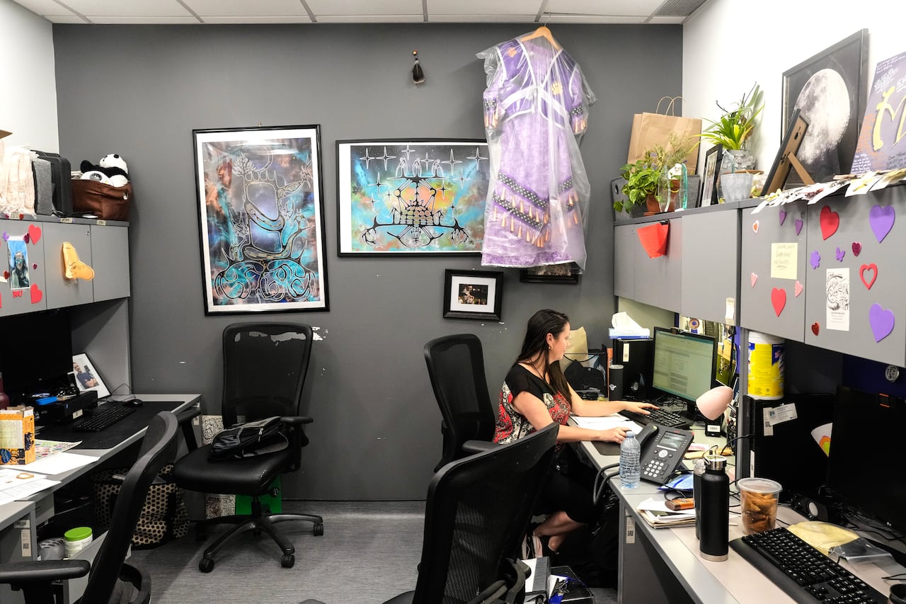 A wide shot of a woman typing a report on a computer at her desk.