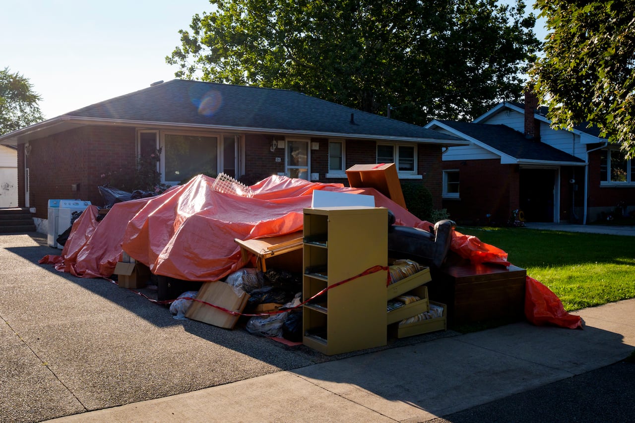 Furniture and debris is piles on the front driveway of a bungalow.