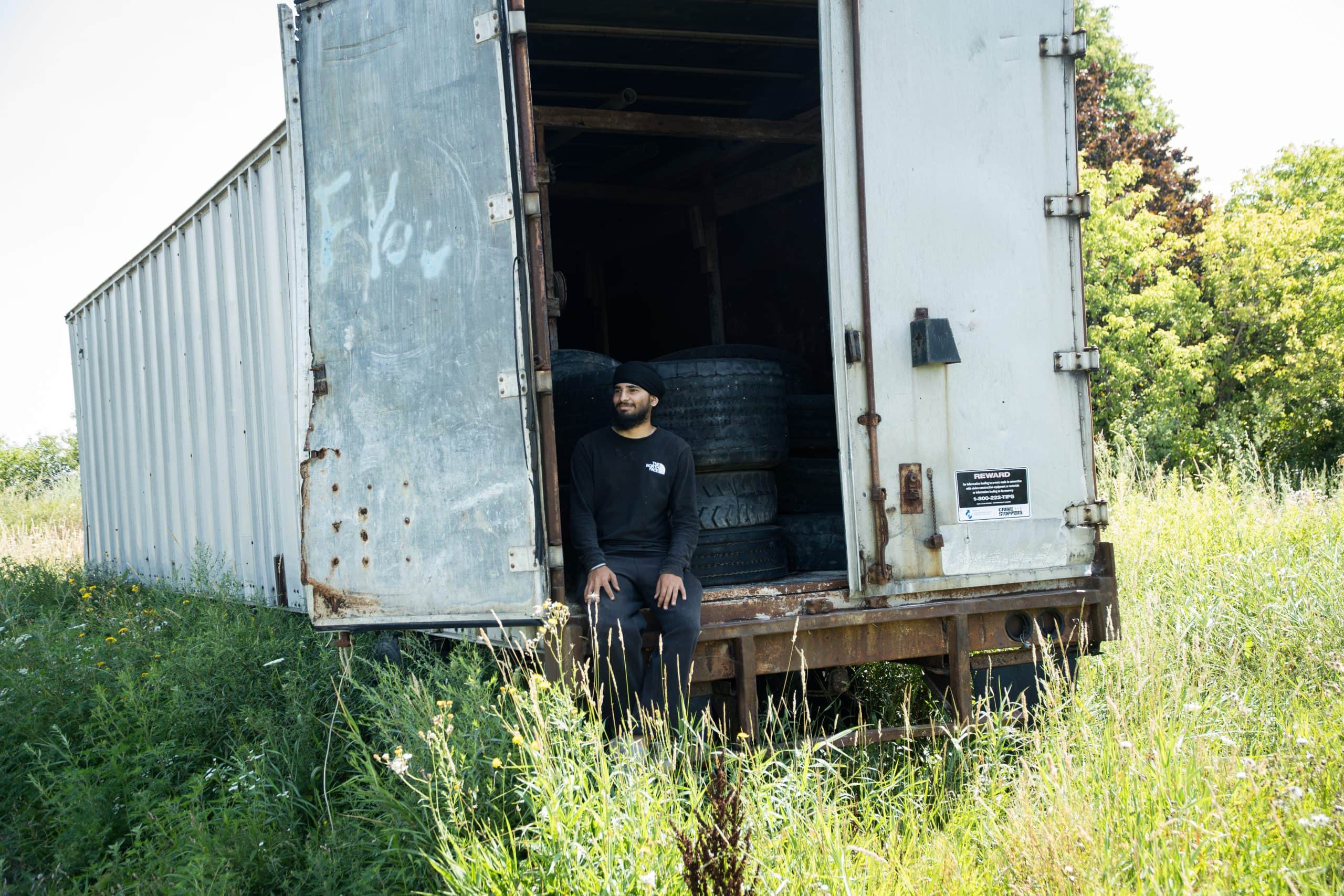 A young man wearing turban sitting inside truck trailer filled tires 