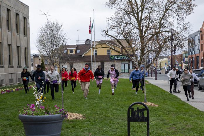 The Amazing Race Canada contestants race past Peterborough City Hall located downtown Peterborough during the fifth episode of season 12 which was filmed around Peterborough and Kawarthas between April and May 2026. Throughout this episode pairs will tackle tasks at various locations including The Canadian Canoe Museum, Ontario Turtle Conservation Centre, Kawartha Dairy among others. (Photo: Bell Media)