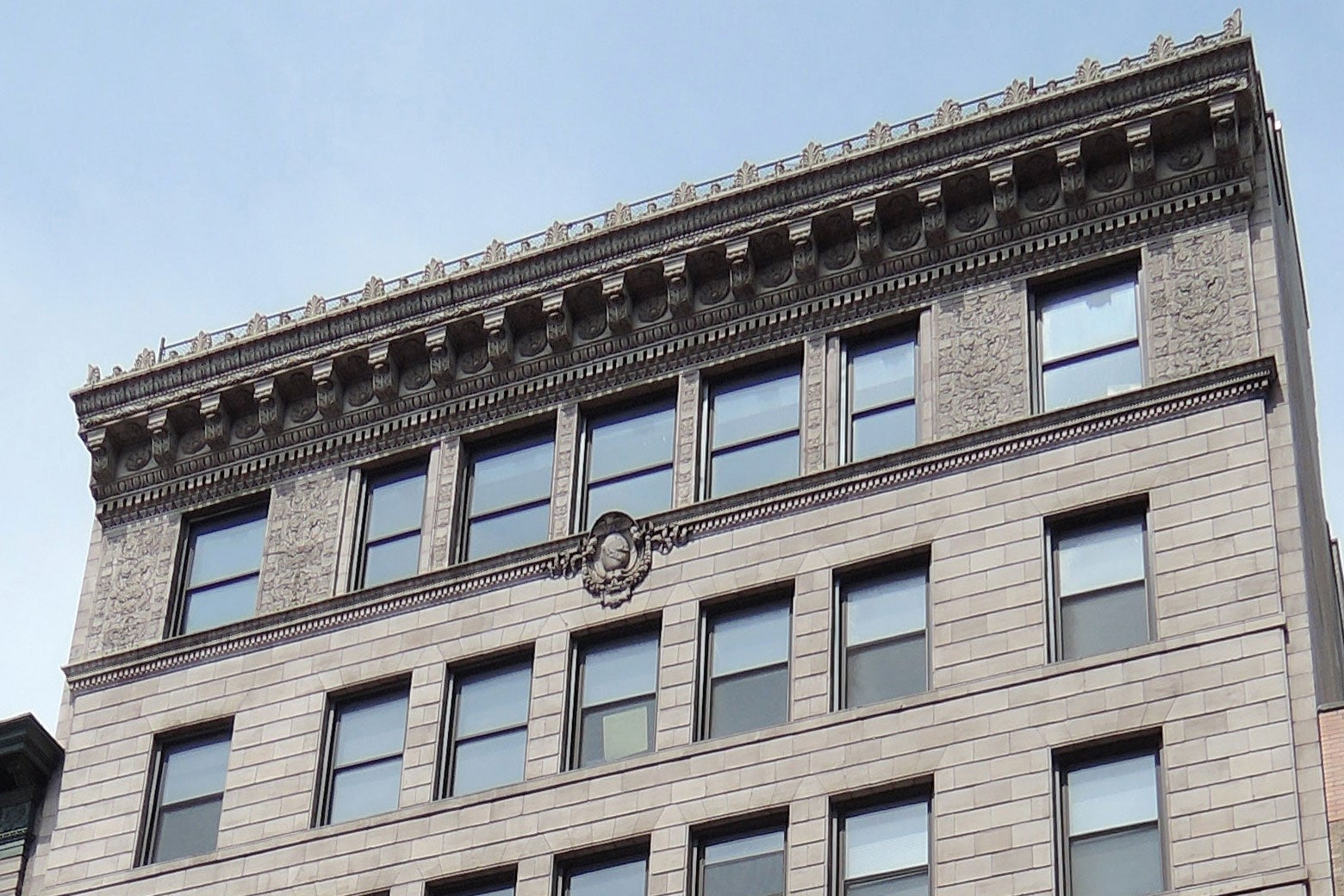 The top three floors of a gray brick building with lots of architectural decoration at the top.